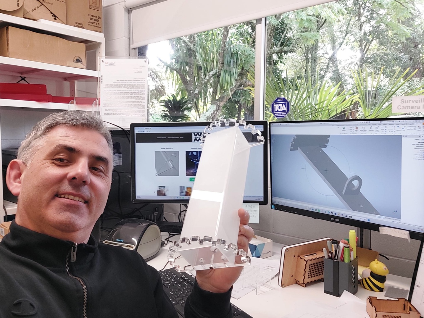 WALMONT product designer holding an acrylic prototype beside a CAD model on a computer screen
